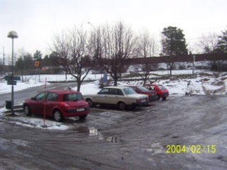 Bild på en parkering med fyra bilar och lite väg bakom i snö